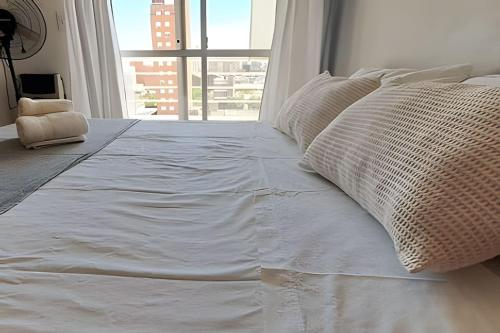 Cama blanca con almohadas en una habitación con ventana en Hornera San Juan - Luminoso Apartamento con Balcón en Rosario