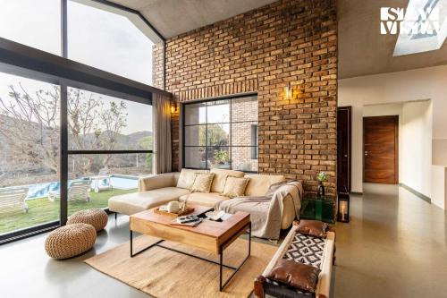 a living room with a couch and a brick wall at StayVista's Ikebana - Living By The Forest Edge - Mountain-view Villa with Infinity Pool, Lawn, & Indoor-Outdoor Games in Udaipur