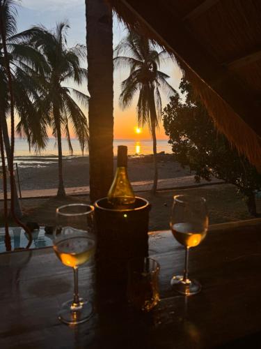 three glasses of wine sitting on a table with the beach at The Beach House Ocam Ocam in Busuanga