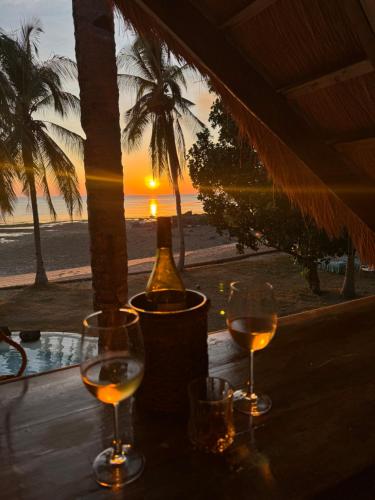 two glasses of wine sitting on a table with the beach at The Beach House Ocam Ocam in Busuanga