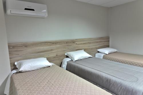 three beds in a room with white walls at Hotel Guerra - Pousada Montebelo in Jaguaruna