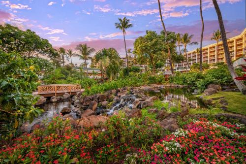 Grand Wailea Resort Hotel & Spa, A Waldorf Astoria Resort في ويليا: جسر فوق شلال في حديقة بها زهور