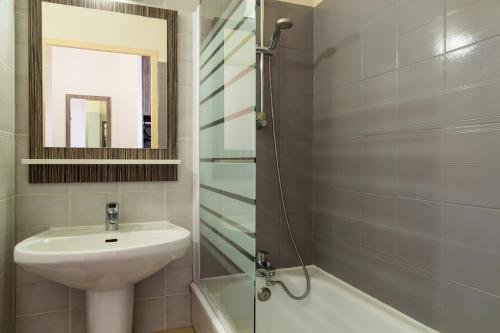 a bathroom with a sink and a mirror and a shower at The Originals City, Hôtel L'Acropole, Saint-Etienne Sud (Inter-Hotel) in La Ricamarie