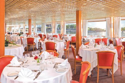 un restaurant avec des tables blanches, des chaises et des fenêtres dans l'établissement Bateau Seine Princess by CroisiEurope, à Paris