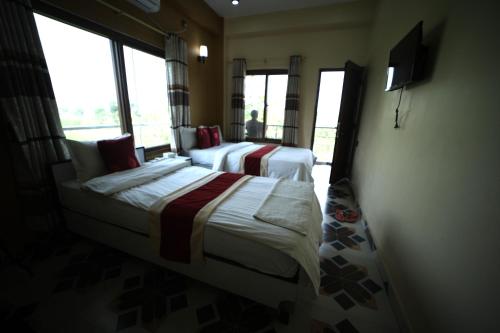 a bedroom with two beds and a tv and windows at Hotel Flycatcher Chitwan in Sauraha