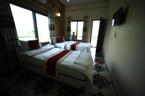 una camera con due letti, una TV e finestre di Hotel Flycatcher Chitwan- A jungle Safari Home a Sauraha