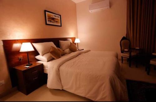a bedroom with a large bed with two lamps and a chair at Ambassador Hotel Clifton in Karachi
