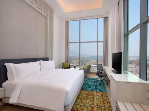 a bedroom with a large bed and a desk with a television at Grand Mercure Lampung in Bandar Lampung