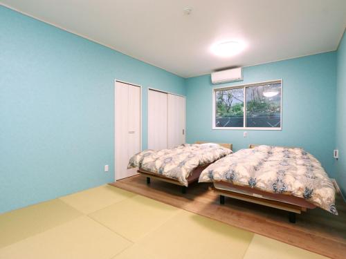 two beds in a room with blue walls and a window at 神津島民宿菊乃屋～きくのや～kikunoya in Kōzushima
