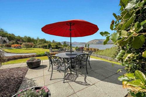 uma mesa e cadeiras com um guarda-sol vermelho num pátio em Outlander Glencoe at Creag an-t Sionnaich em Glencoe