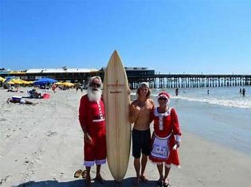 three people dressed in santa costumes standing on a beach with a surfboard at Sunny Delight I in Cape Canaveral