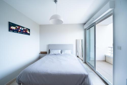 une chambre blanche avec un lit et une grande fenêtre dans l'établissement L'Oiseau Bleu - Vue mer montagne, 100m de la plage, à Canet
