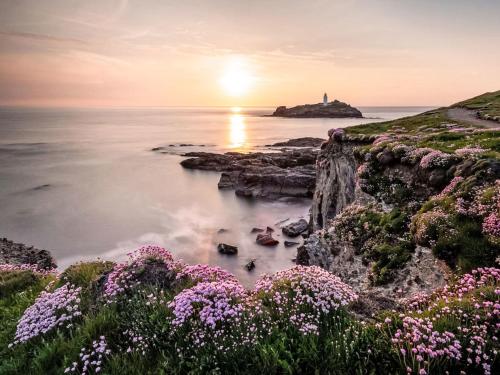 a sunset over the ocean with a lighthouse and flowers at Apartment Lighthouse View by Interhome in Mevagissey