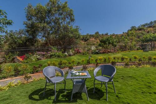 two chairs and a table in a garden at SaffronStays Caramelo - a private heated swimming pool villa with Jacuzzi nestled amidst beautiful landscaping and gardens in Lavasa in Lavasa