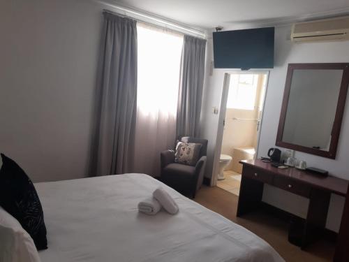 una camera d'albergo con letto, sedia e specchio di Sapphire Hotel Halevy Heritage a Bloemfontein