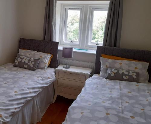twee bedden in een slaapkamer met twee ramen bij Cosy home in an area of outstanding natural beauty in Wookey Hole