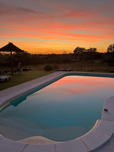 an empty swimming pool with a sunset in the background at Monte da Masmorra de baixo-Casa Alentejana in Montemor-o-Novo