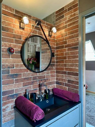 La salle de bains est pourvue d'un lavabo et d'un miroir sur un mur en briques. dans l'établissement Camélia, à Bayeux