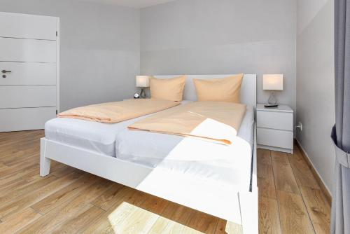 a white bed in a white bedroom with wooden floors at Residenz Waterkant in Bensersiel