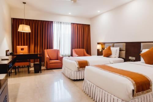 una camera d'albergo con 2 letti e una scrivania di The Alcor Hotel a Jamshedpur
