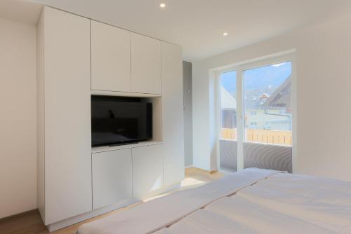a white bedroom with a tv on a wall at Apartments BB in Bohinj
