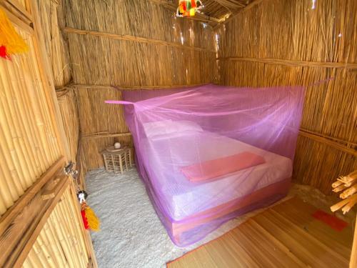 a bed in a wooden shack with a purple mosquito net at Paloma Camp in Siwa