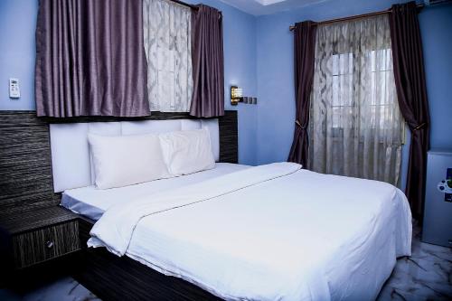 a white bed in a blue room with a window at MO-House Hotels and Apartments Mabushi in Abuja