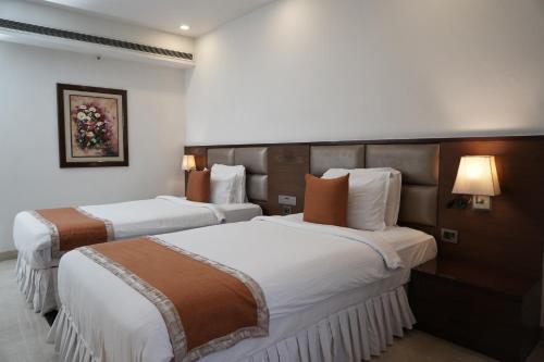 two beds in a hotel room with white and brown at The Alcor Hotel in Jamshedpur