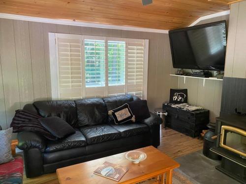 sala de estar con sofá de cuero negro y TV en Ada Lake Cottage - Port Carling couples retreat, en Port Carling
