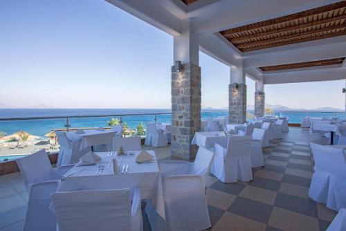 a banquet hall with white tables and chairs and the ocean at Grand Blue Beach Hotel in Kardamaina