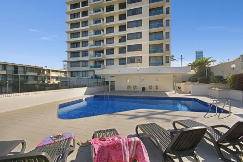 a swimming pool with chairs and a building at Burgess @ Kings Beach Apartments in Caloundra