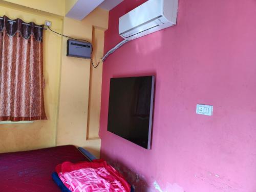 Habitación con pared de color rosa y TV de pantalla plana. en Hotel Shobha and Tent House en Patrātu