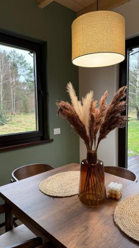 a dining room table with a vase with feathers on it at Leśna Osada na Kaszubach - drewniane domy na wynajem in Bartoszylas