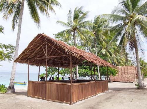 a straw hut on the beach with palm trees at Mamere Homestay Raja Ampat in Fam