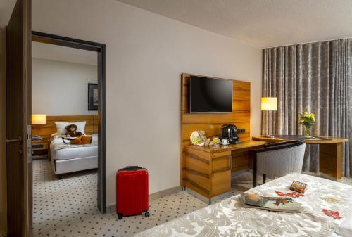 a hotel room with a bed and a desk with a red suitcase at Maritim Hotel Bad Homburg in Bad Homburg vor der Höhe