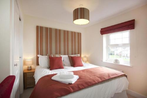 a bedroom with a large bed with red pillows and a window at DBS Serviced Apartments - The Stretton in Castle Donington