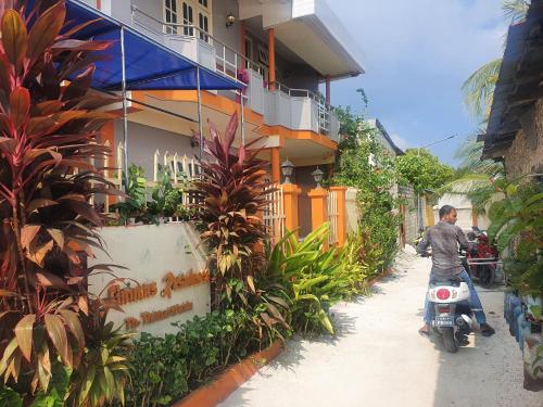 a man riding a motorcycle down a street next to a building at Finimas Residence in Thimarafushi