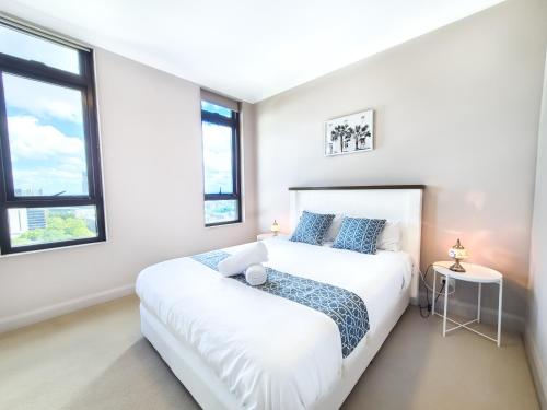 a white bedroom with a bed and two windows at Holiday Style 2 BRStudy Apartment in Olympic Park in Sydney
