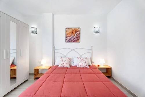 a red bed in a white room with two tables at Apartamento La Concha in Candelaria