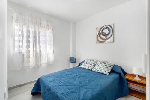 a white bedroom with a blue bed and a window at Apartamento La Concha in Candelaria