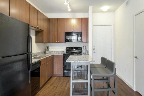 een keuken met houten kasten en een zwarte koelkast bij Landing at Axis Waterfront - 1 Bedroom in Downtown Benbrook in Fort Worth