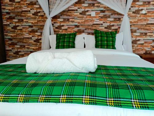 uma cama com um cobertor e almofadas verdes e brancas em Queen's Way Resort em Kisumu
