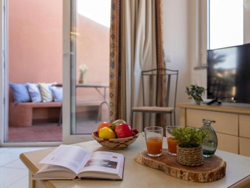 una mesa con un libro y un bol de fruta y zumo en Apartment Cala Rossa 1505 by Interhome, en Trinità dʼAgultu