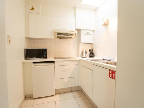 cocina blanca con armarios blancos y microondas en Apartment Koekoeksnest by Interhome, en De Haan