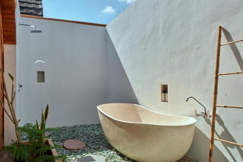 La salle de bains est pourvue d'une baignoire dans un mur blanc. dans l'établissement Plumeria NP, à Nusa Penida