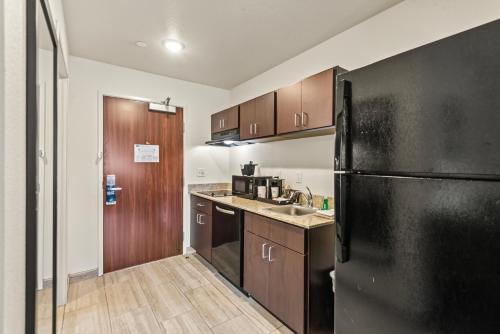 a kitchen with a black refrigerator and wooden cabinets at Riverstone Suites by Cobblestone Hotels - Chippewa Falls in Chippewa Falls