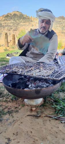 a man is sitting in front of a grill at oasis panorama in Bawiti