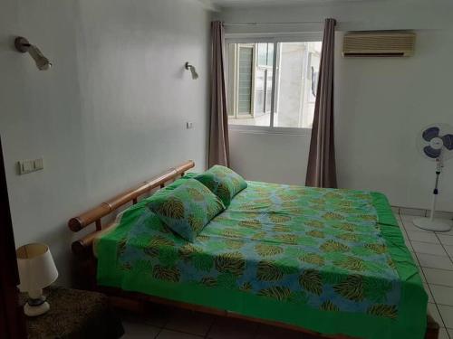 a bedroom with a bed with a green comforter and a window at F3 Papeete centre-ville in Papeete