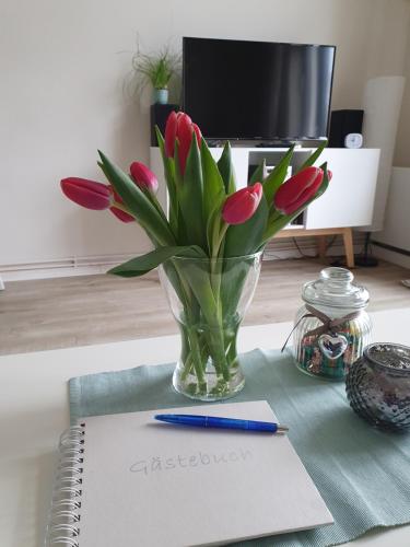 wazon czerwonych tulipanów siedzących na stole z notesem w obiekcie Ferienwohnung Stadtvilla - charmante Gemütlichkeit w mieście Bad Oldesloe