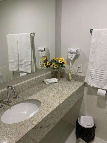 a bathroom with a sink and a mirror and flowers at Apartamento Hotel Itaipava Petropolis in Petrópolis